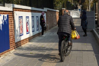 Tahran, İran - Kasım 2019. Yaşlı bir adam bisikletiyle İran 'daki eski Amerikan elçiliğinin önünden geçiyor..