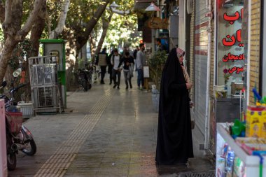 İsfahan, İran - Kasım 2019. Siyah Chador 'lu bir kadın Grand Bazaar' da dükkana giriyor. İnsanlar arka planda kaldırımda yürüyorlar..