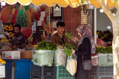 İsfahan, İran - Kasım 2019. Açık hava sebze dükkanı. Kadın genç bir satıcıdan nane ve fesleğen alır..