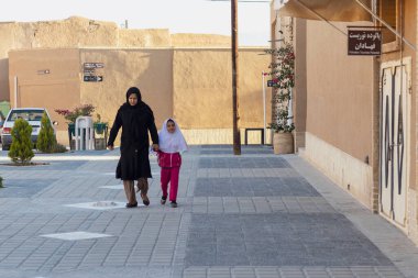 Yazd, İran - Kasım 2019. İranlı bir kadın kızına okula kadar eşlik ediyor. Beyaz tesettürlü bir kız öğrenci, siyah çarşaflı annesi..