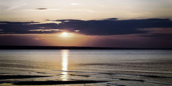 Hermoso paisaje ardiente de la puesta de sol sobre el mar y el cielo naranja por encima de él con increíble reflejo dorado del sol en las olas tranquilas en el fondo . — Foto de Stock