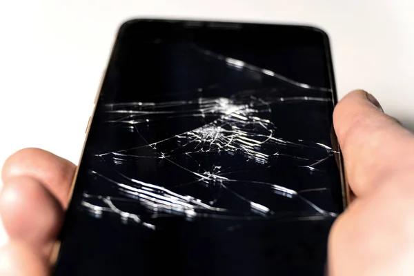 Phone in hand, screen cracked. Broken smartphone glass. Phone repair. Selective focus of cracks on the screen
