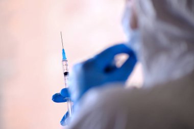 Yorgun bir doktor elinde ilk yardım şırıngası tutuyor. Şırıngada virüse karşı bir aşı var..