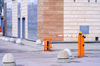 Beton yol bariyerleri ve turuncu renkli, beyaz çizgili ve kırmızı uyarı şeritli, arabaların girişi için basınçlı bariyer. Seçkin bir yerleşim yerinin avlusuna giriş.