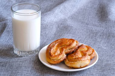 Çuval bezinin arka planında bardaktaki süt. Bir fincan tabağında taze pişmiş tatlı rulo. Doğal ürün. İzole edilmiş arka plan. Süt içeceği. Süt damlası.