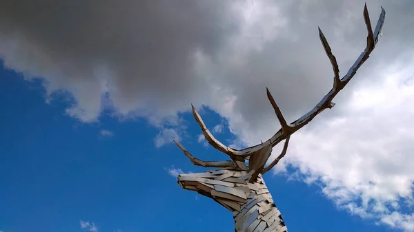 metallic figure of a deer\'s head against a cloud