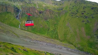 Dağların arkasında kırmızı teleferik kabini
