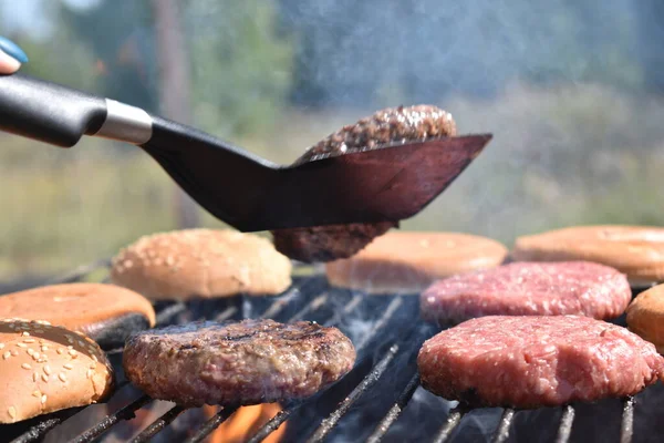 the process of making burgers on the grill in the garden