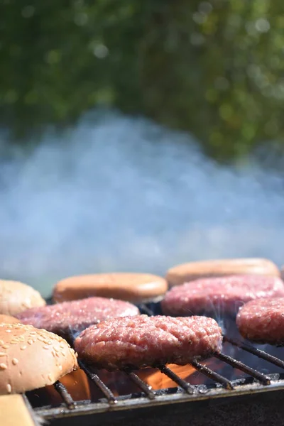 the process of making burgers on the grill in the garden