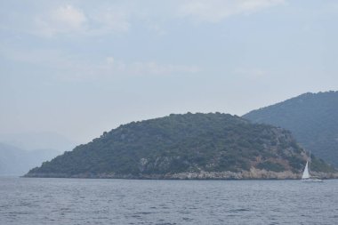 Beyaz yelkenli bir yat, dağların arka planına karşı denizde ilerliyor.