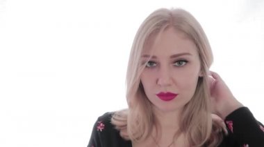 Kırmızı dudaklı çekici sarışın kadın kameraya bakıyor ve saçıyla oynuyor. Baştan çıkarma, güzellik. Beyaz arka plan. Seksi görünüş.