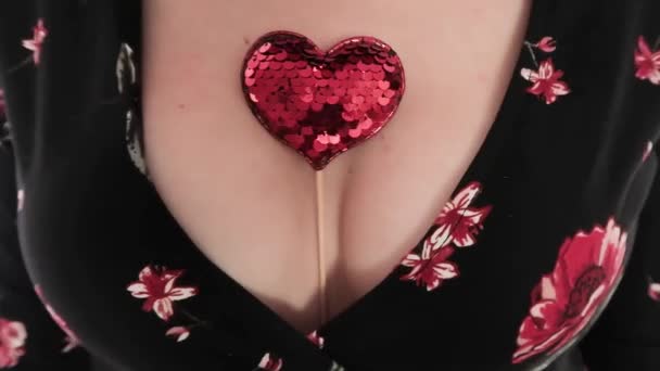 Large female breast, deep neckline. Shiny red heart with sequins, sandwiched between breasts. Seduction — Stock Video