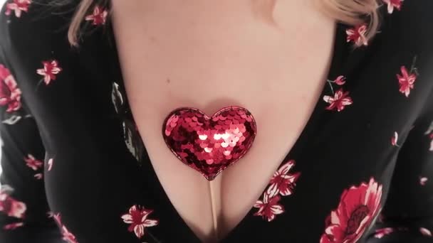 Ярко-красное сердце на палочке между большой грудью в глубокой декольте — стоковое видео