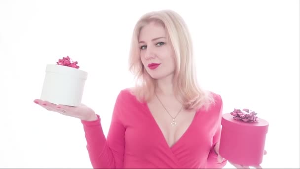 Mooie sexy jonge blonde vrouw in rode jurk met open borst en rode lippenstift houdt twee geschenkdozen. weeg de doos en kies rood. Opent en glimlacht teleurgesteld. — Stockvideo