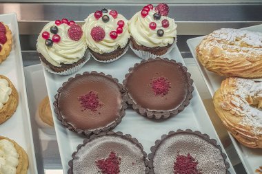 Farklı dolgulu kekler ve renkli jöle, vitrinin arkasında meyve ve böğürtlenlerle süslenmiş, tatlı tatlı