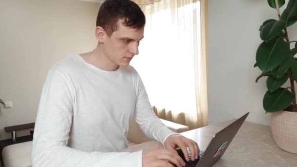 Young man is typing something on a laptop, then leans back, throws his hands behind his head and smiles pretty, concept of remote work, business — Stock Video