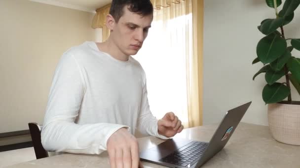 Ein junger Mann Freiberufler verschiebt Smartphone und drucken etwas auf dem Laptop, das Konzept der Fernarbeit, Handlungsfreiheit, Geschäft — Stockvideo
