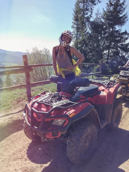 Mladá žena v helmě na čtyřkolce na pozadí lesa a plotu — Stock fotografie