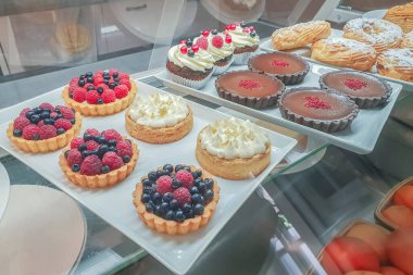 Farklı dolgulu kekler ve renkli jöle, vitrinin arkasında meyve ve meyvelerle süslenmiş, tatlı ve renkli tatlı.