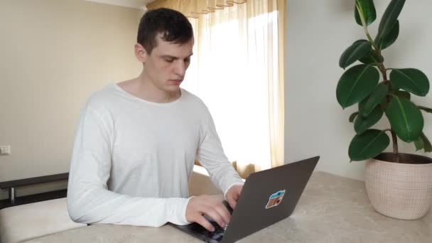 Seriöser junger Mann tippt etwas auf den Laptop, blickt dann in die Kamera, Fernbedienung, Online-Kommunikation — Stockvideo