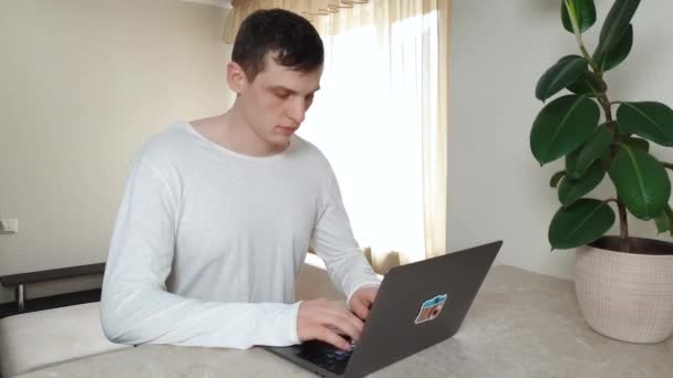 Joven hombre guapo trabajando con el ordenador portátil en casa, el concepto de freelancing — Vídeos de Stock