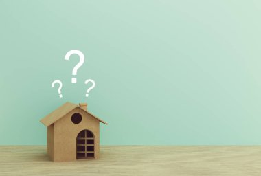 Kağıt ev modeli. Ahşap masa üzerinde soru işaretleri var.