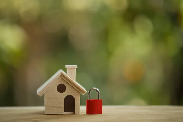 Home security concept: Wooden model house and red key lock on wooden table. Dangers that may occur in the home. And taking care of home safety for everyone in the family