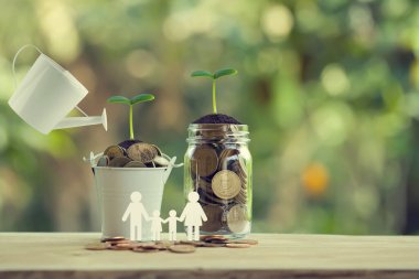 Bankacılık ve finans, tasarruf konsepti: Su, cam şişe ve aile üyeleriyle dolu kova dolusu parayla yeşil filizlerin üzerine dökülüyor. Büyümek için para yatırımı tasvir ediyor.