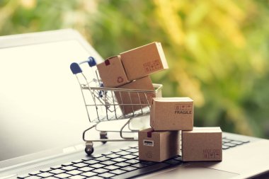 Defter klavyesindeki alışveriş arabasındaki karton kutular. E-ticaret veya elektronik ticaret hakkındaki fikirler İnternet üzerinden mal veya hizmet satın alma veya satma işlemidir..