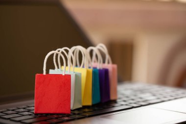 Not defteri klavyesinde renkli kağıt alışveriş torbaları. Müşterilerin evlerinden ya da işyerlerinden hangi ürünleri, hizmetleri ya da malları satın alabileceklerine dair internet üzerinden alışveriş veya alışveriş fikirleri.