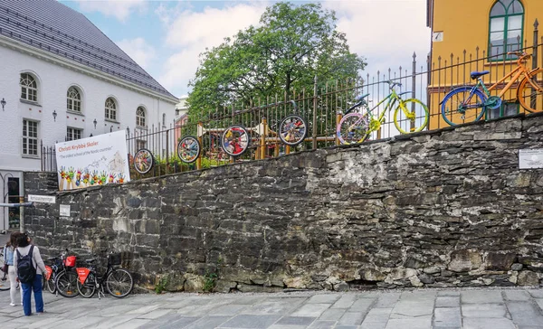 Bergen, Norveç - 22 Temmuz 2018: parlak, renkli bisikletler taş bir duvara yerleştirildi. Turistler serginin yaratıcıları hakkında bilgi okuyorlar.