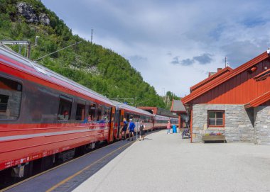 Myrdal İstasyonu, Norveç - Temmuz 2018: Resimli yeşil tepelerin arka planında uzun kırmızı tren. Yolcular biniyor.
