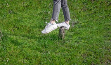 Spor ayakkabılı bacaklar parlak yeşil bir çayırın arasındaki eski bir kütüğün üzerinde duruyor. Her durumda dengeyi koruma kavramı. Büyük boş alan.