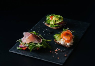 three sandwiches on a black background with avocado fish and ham