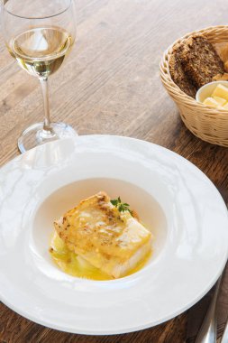 Bir bardak şarap ve ekmek sepetiyle kremalı soslu beyaz balık.