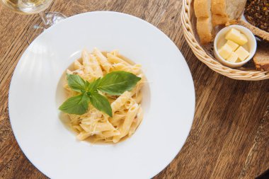Peynirli ve fesleğenli pappardelle bir restorandaki ahşap masada beyaz şarap ve malzemelerin yanında.
