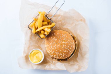 Patates kızartması ve sarı soslu hamburgerler el sanatları kağıdında patates kızartması ve sarı soslu yukarıdan hafif arka plan manzaralı.