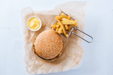 Patates kızartması ve sarı soslu hamburgerler el sanatları kağıdında patates kızartması ve sarı soslu yukarıdan hafif arka plan manzaralı.