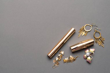 Güzellik ve makyaj arka planında fotokopi alanı var. Altın kozmetik ve gri arka planda küpeler.