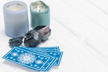 Mavi tarot kartları ve yanan mum beyaz masa arka planında.