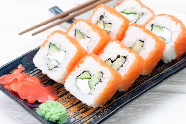 Suşi Philadelphia 'yı tabakta yuvarlıyor, beyaz ahşap masanın üstünde..