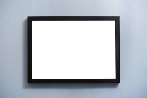 Blank empty photo frame with copy space hanging on the blue wall background.