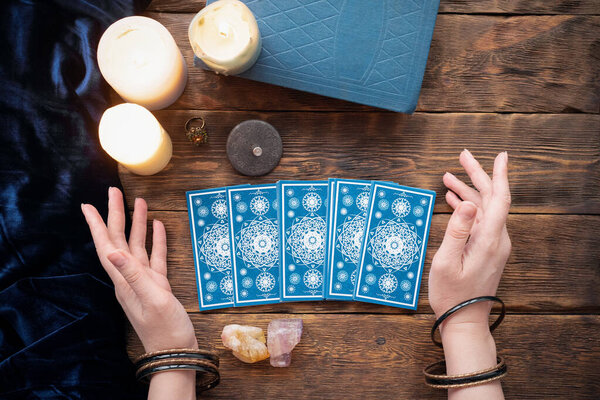 Fortune teller with tarot cards in the hand on brown table background.