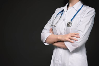 Steteskoplu doktor çapraz kollarıyla duruyor. Koyu arkaplanda fotokopi alanı ile yakın plan..