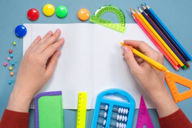 Öğrenci not defterine mavi düz zemin üzerinde kalem ve okul aksesuarlarıyla kopya alanı ile yazı yazıyor. Okul konseptine dönelim..