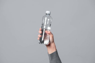 Kadın ellerinde bir şişe su. Gri arka plana yakın plan..