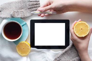 Fotokopi alanı olan boş ekranlı dijital tablet, beyaz masa zemininde termometresi olan sıcak çay, limon ve el..