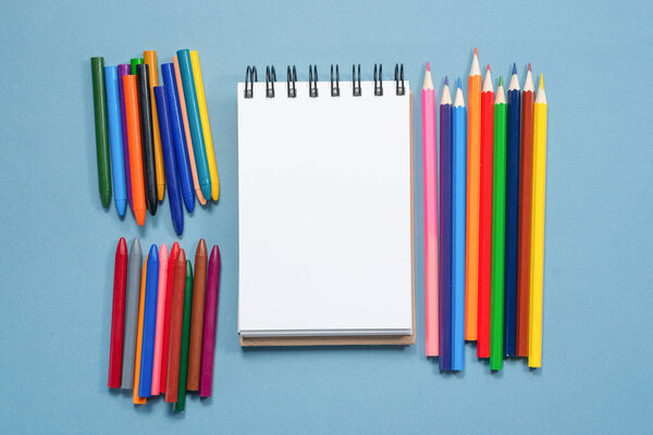 Colorful pencils and blank paper page with copy space on blue background.