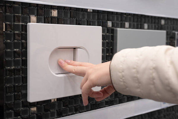 Female hand pressing a toilet flush button on the wall.