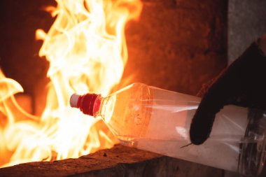 Elle tutuşan bir sıvı şişeyle eldiven ve şöminenin arka planında yanan ateş yakın..